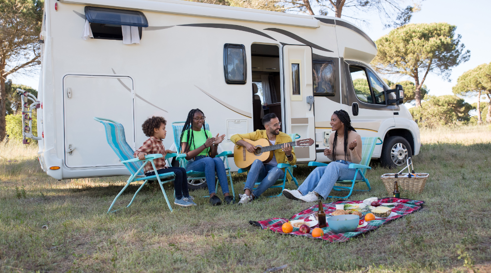 A family with their RV sitting around playing music and having a picnic.